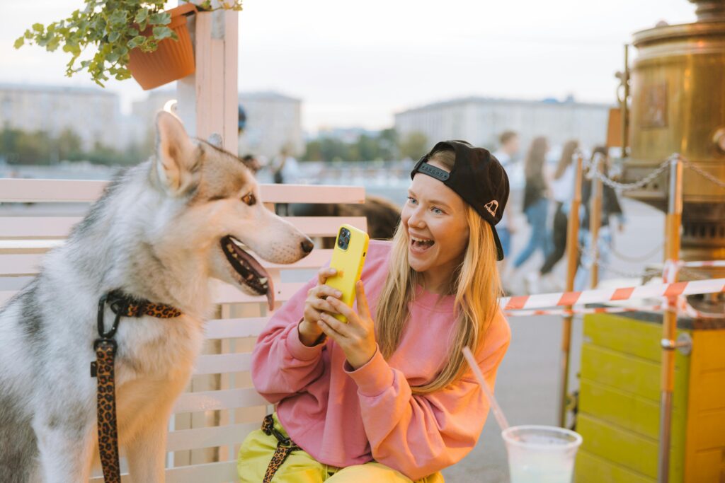 Smiling young woman in a pink shirt taking a selfie outdoors with her Siberian husky.